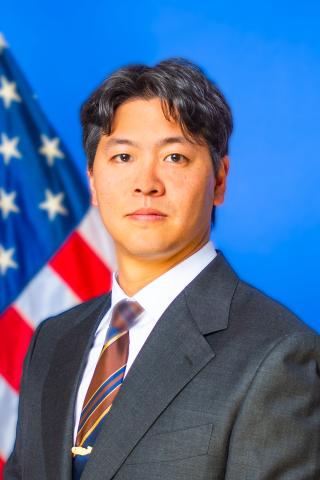 Man in suit and tie stands in front of the American flag.