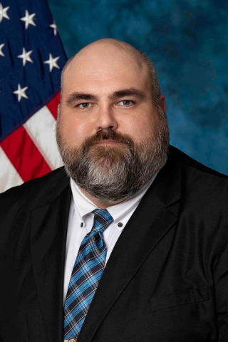Man in suit and tie with American flag in background.