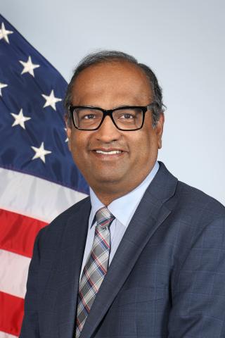 Man in suit and tie standing in front of an American flag.