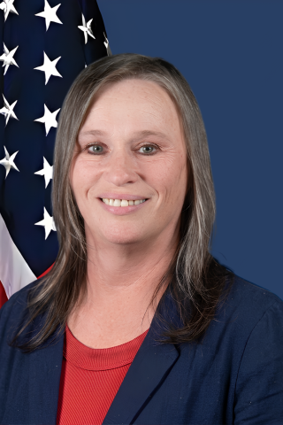 Woman with gray hair smiling in front of American flag.
