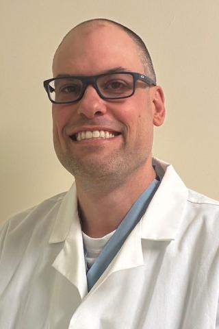 Bald man in white lab coat and glasses smiling.
