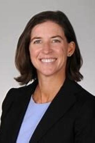 Woman in black blazer and blue shirt smiling at the camera.