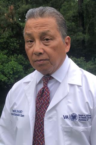 Headshot of an older man in a white lab coat and red necktie.