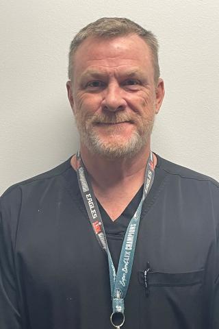 Man with gray hair and beard, wearing a black shirt and green lanyard.