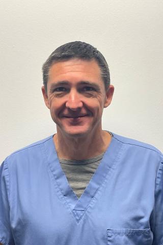 Portrait of a smiling man in blue scrubs against a plain white background.