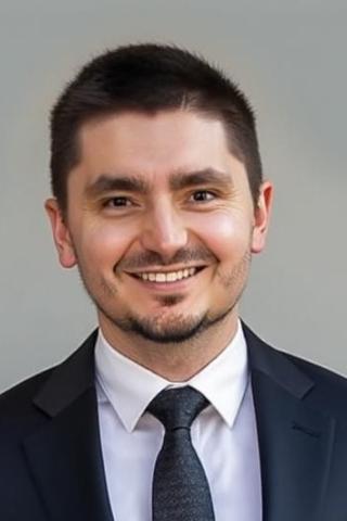 A smiling man in a black suit and tie poses for a photo.