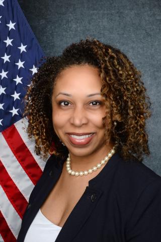 Woman with curly hair smiling in front of American flag.