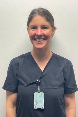 Smiling woman in dark blue scrubs with a light blue ID badge.