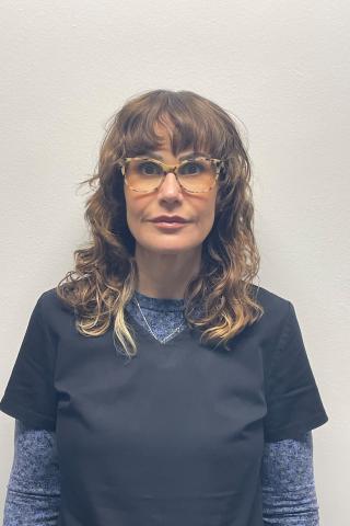 Woman with curly hair wearing glasses and a dark blue shirt.