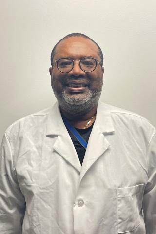 Man in white lab coat and glasses smiles against plain white background.