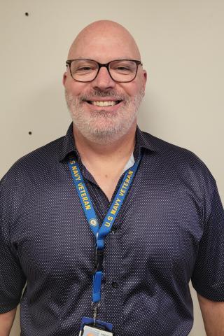 Smiling bald man with glasses and a blue lanyard.