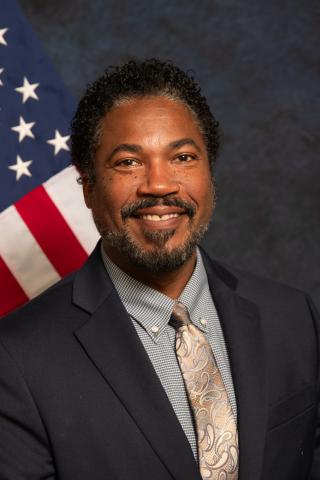 Man in a suit with a flag in the background.