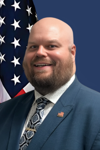 Portrait of bald man in suit and tie smiling by American flag.