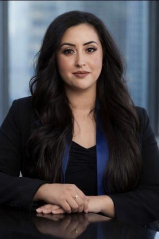 A professional portrait of a woman in a black blazer and blue scarf smiling.