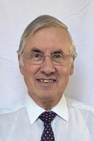 Photo of an elderly man with glasses, wearing a light blue shirt and a polka dot tie.