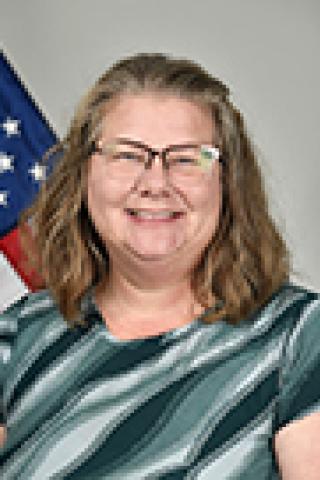 Woman with glasses smiling with US flag in background.