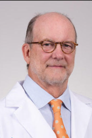 Photograph of a smiling man wearing glasses, a blue shirt, and a white lab coat with an orange tie.