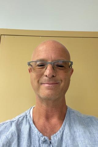Portrait of bald man with glasses smiling in front of a yellow door.