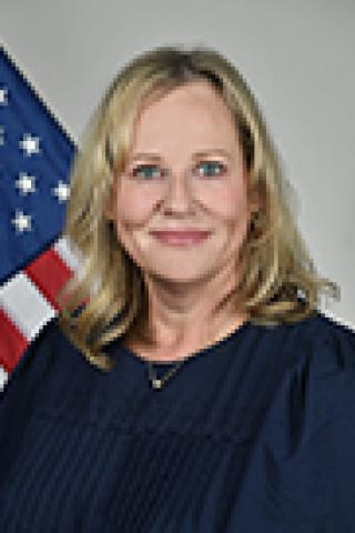Blonde woman smiling in front of an American flag.