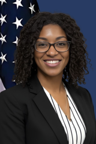 Woman in business attire smiling in front of American flag.