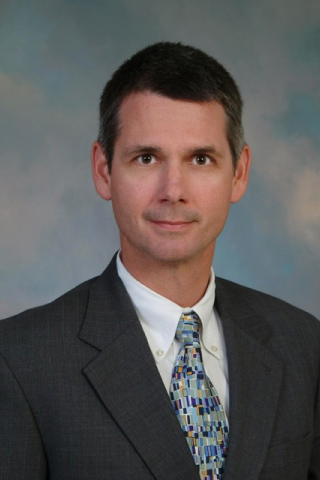 Professional headshot of a man in a gray suit and colorful tie.