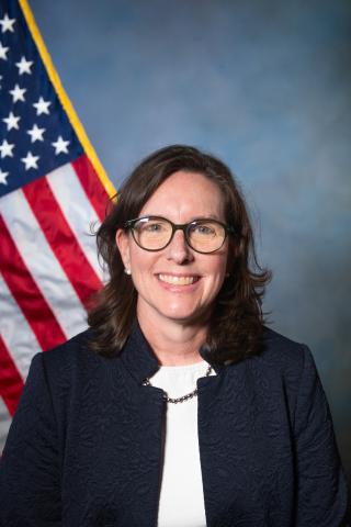 Portrait of a smiling woman with glasses in front of a US flag.