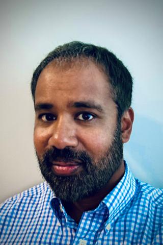 Portrait of a man with a beard wearing a blue and white checkered shirt.