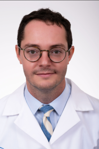Smiling man in a white lab coat and blue tie with white stripes.