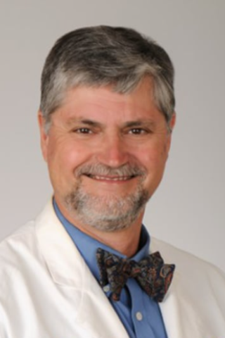 Smiling man in white lab coat and bowtie, headshot.