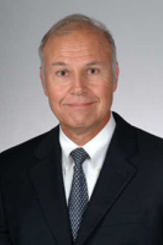 Headshot of a smiling man in a suit and tie against a gray background.