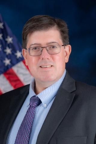 Man in suit and tie standing in front of American flag.