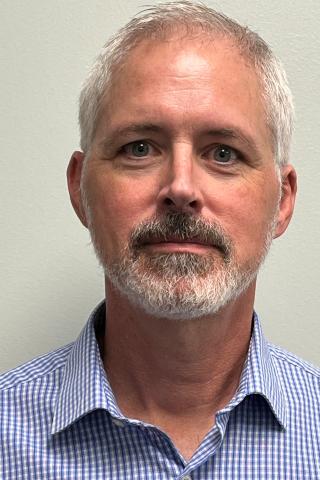 Man with white hair, beard, and mustache, wearing blue shirt.