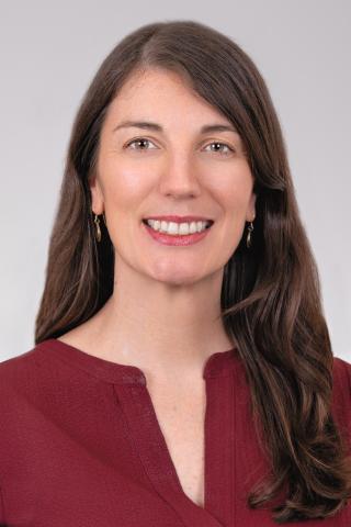 Portrait of a woman with long brown hair wearing a maroon shirt, smiling.