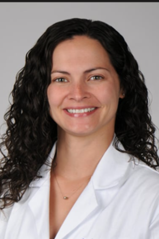 Woman with curly black hair and white lab coat smiling at camera.