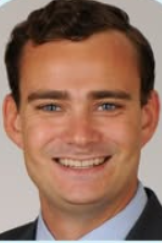 Headshot of a smiling man in a suit with blue shirt.