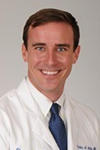 Portrait of a smiling man in a white lab coat and blue tie.