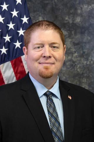 Man in suit and tie smiling in front of American flag.