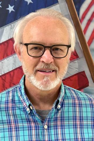 Headshot of a man with an American flag in the background.