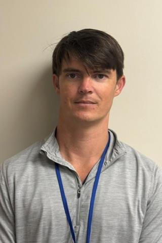 Headshot of a man in a gray polo shirt with a blue lanyard.