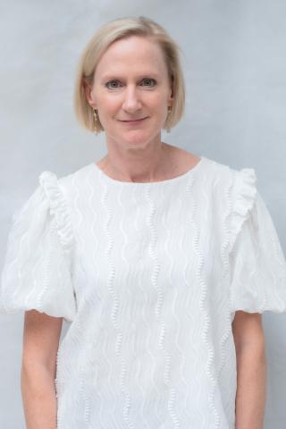 Portrait of a smiling woman with short blonde hair wearing a white blouse.