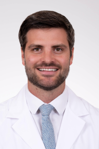 Man with short hair and beard in white lab coat and blue tie smiling.