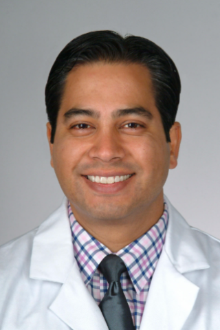 Man in a white lab coat and tie smiling for the camera.
