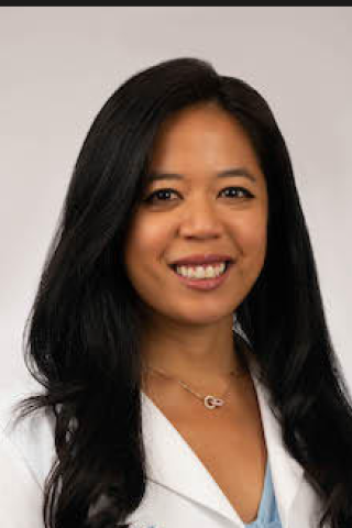 A smiling woman with long black hair, wearing a white lab coat and necklace.
