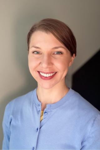 Portrait of a smiling woman in a blue shirt against a light background.