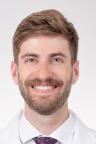 Portrait of a smiling man in white shirt and purple tie.