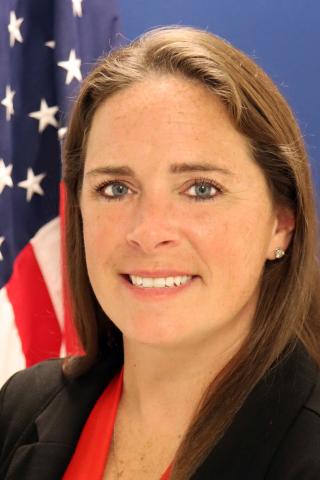 female, brown hair in front of American flag