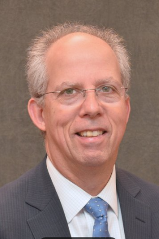 Man in a suit and blue tie smiling for the camera.
