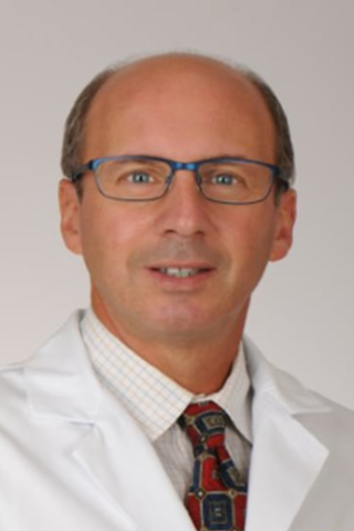 Man in white lab coat, blue tie, and glasses smiling for photo.