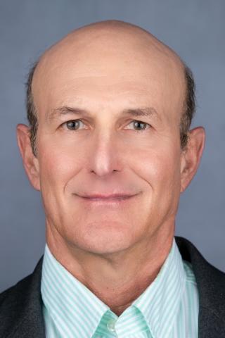 Headshot of a smiling bald man in a striped shirt and jacket.