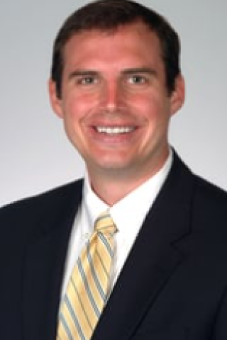 Man in black suit and yellow striped tie smiling.